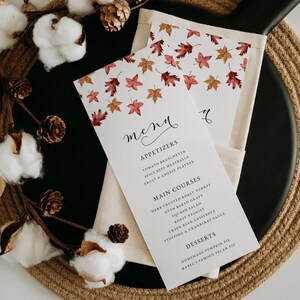 May include: A menu card with a fall theme, featuring a leaf pattern in red, orange, and brown. The word "menu" is written in elegant script. The menu lists appetizers, main courses, and desserts, including pumpkin pie.