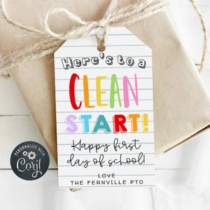 May include: A gift tag with the text "Here's to a CLEAN START! Happy first day of school!" in colorful letters. The tag is white with blue lines, and the gift is wrapped in brown paper with twine.