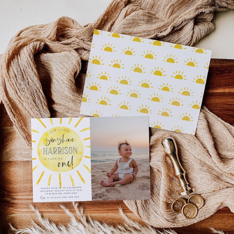 May include: A rectangular birthday invitation card featuring a yellow sun graphic with the text Our Little Sunshine Harrison Is Turning One, including event details and a photograph of a child on a beach, paired with a matching sun-patterned card.
