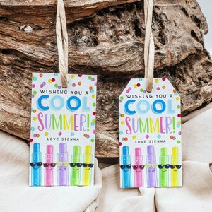 May include: Two gift tags with the text "Wishing you a COOL SUMMER!" and "Love Sienna." The tags feature colorful cartoon-style illustrations of sunscreen bottles wearing sunglasses. The tags are hanging from a natural fiber string.
