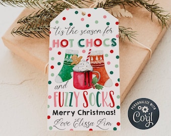 Pode incluir: Uma etiqueta de presente de Natal com um design vermelho, verde e branco. Apresenta uma caneca de chocolate quente com chantilly e um homem de gengibre, juntamente com um par de meias felpudas. O texto diz "Tis the season for hot chocs and fuzzy socks. Merry Christmas! Love Elissa Lim".