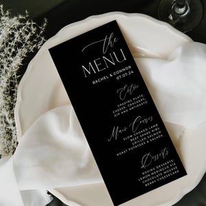 May include: Black and white wedding menu card with the text "The Menu" in a script font. The menu lists the names Rachel & Connor and the date 07.07.24. The menu includes appetizers, main courses, and desserts.