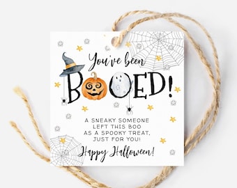 May include: A white tag with a black and white spiderweb design. The tag has the text "You've been BOOED!" with a pumpkin and ghost illustration. The text continues with "A sneaky someone left this boo as a spooky treat, just for you! Happy Halloween!"