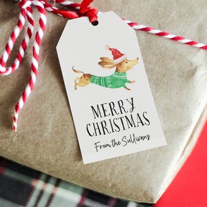 May include: A white gift tag with a cartoon dachshund wearing a green sweater and a red Santa hat. The tag says "Merry Christmas" and "From the Sullivans".