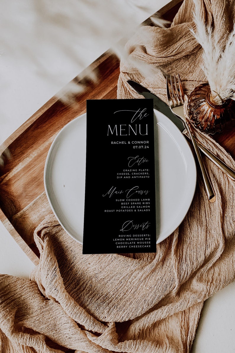 May include: A black menu card with white text. The menu card lists the menu for a wedding reception with the title "The Menu" and the names Rachel & Connor and the date 07.07.24. The menu includes appetizers, main courses, and desserts.