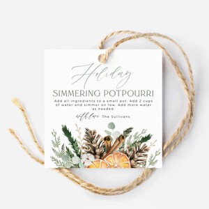 May include: A white gift tag with a green and brown watercolor illustration of pine cones, cinnamon sticks, and orange slices. The text on the tag reads "Holiday Simmering Potpourri Add all ingredients to a small pot. Add 2 cups of water and simmer on low. Add more water as needed. with love The Sullivans"