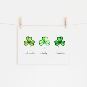 May include: Three watercolor shamrock illustrations with the words "charmed", "lucky", and "blessed" written underneath each shamrock.