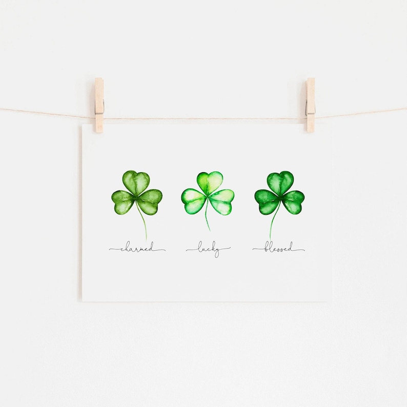 May include: Three watercolor shamrock illustrations with the words "charmed", "lucky", and "blessed" written underneath each shamrock.