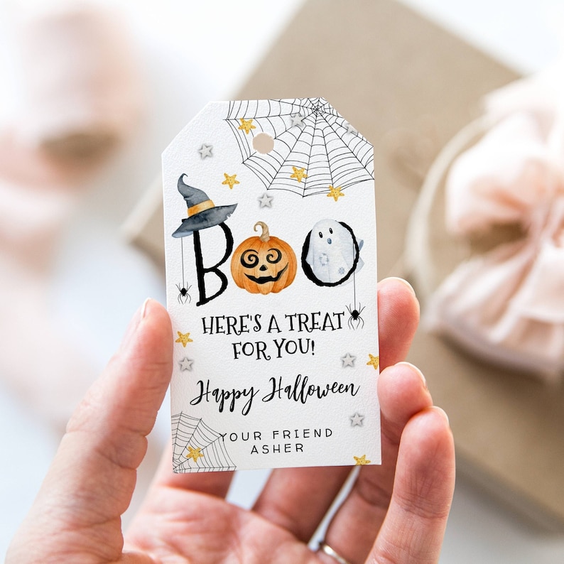 May include: White gift tag with a black spiderweb, gold stars, and a ghost, pumpkin, and witch hat illustration. The text reads "BOO! HERE'S A TREAT FOR YOU! Happy Halloween YOUR FRIEND ASHER".