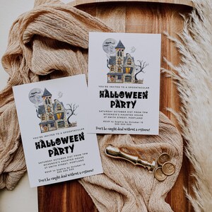 May include: Two white invitation cards with black text and a cartoon illustration of a haunted house. The text reads "You're invited to a Spooktacular Halloween Party" and includes the date, time, location, and RSVP information. The text also says "Don't be caught dead without a costume!"