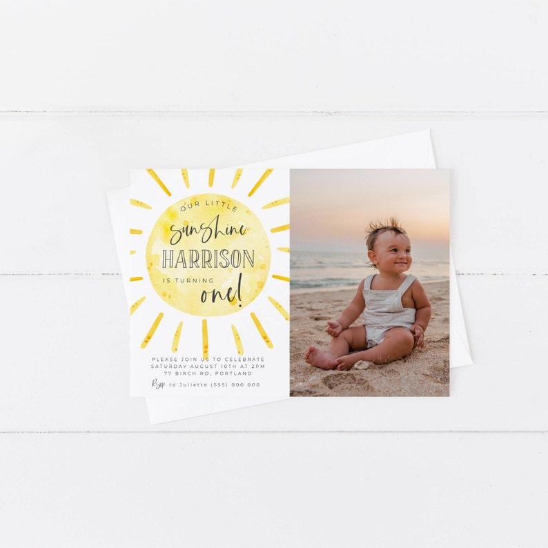 May include: A rectangular birthday invitation card featuring a yellow watercolor sun graphic with the text Our little sunshine HARRISON is turning one. The card includes a photograph of a child sitting on a sandy beach at sunset and event details.