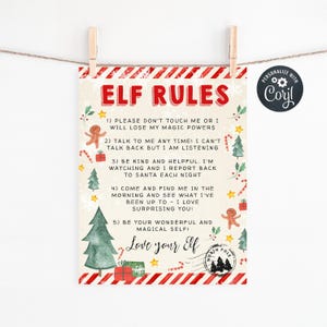 May include: A festive Elf Rules sign, printed on cream-colored paper and held by wooden clothespins. The sign features red and white striped borders, Christmas tree and gingerbread man illustrations, and the text "ELF RULES" in red. The sign includes five rules for the elf.
