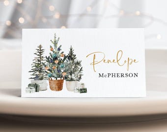 May include: A white Christmas place card with a watercolor illustration of three small Christmas trees decorated with ornaments and lights. The name "Penelope McPherson" is written in gold script.