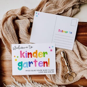 May include: Two white postcards with colorful text and star accents. One card reads Welcome to kindergarten! I'm so glad you're in my class! Love Miss Walsh. The other card features the text Deliver to with lines for an address and a stamp box.