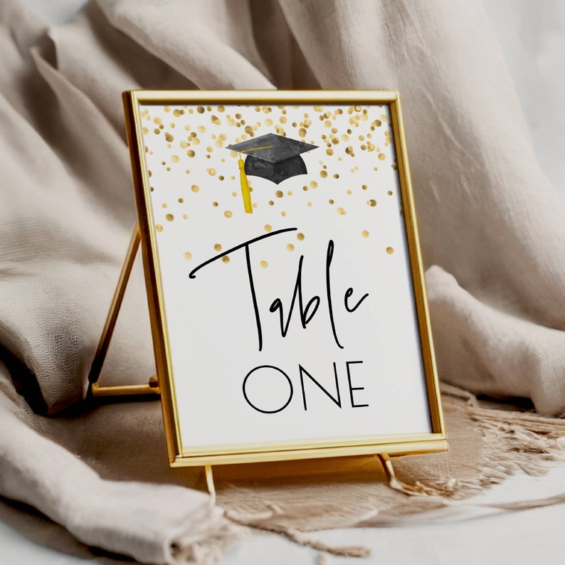 K&ouml;nnte beinhalten: Goldene Tischnummerkarte mit einer schwarzen Abschluss-Kappe und goldenen Konfetti. Die Karte zeigt "Table One" in schwarzer Schrift.