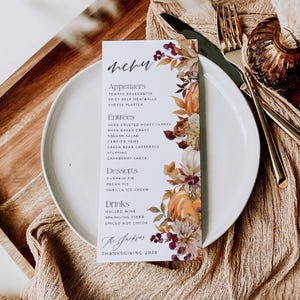 May include: A rectangular white menu card featuring the text Menu, Appetizers, Entrees, Desserts, Drinks, The Jacksons, and Thanksgiving 2026. The right side is decorated with a watercolour illustration of orange pumpkins, autumn leaves, and berries.