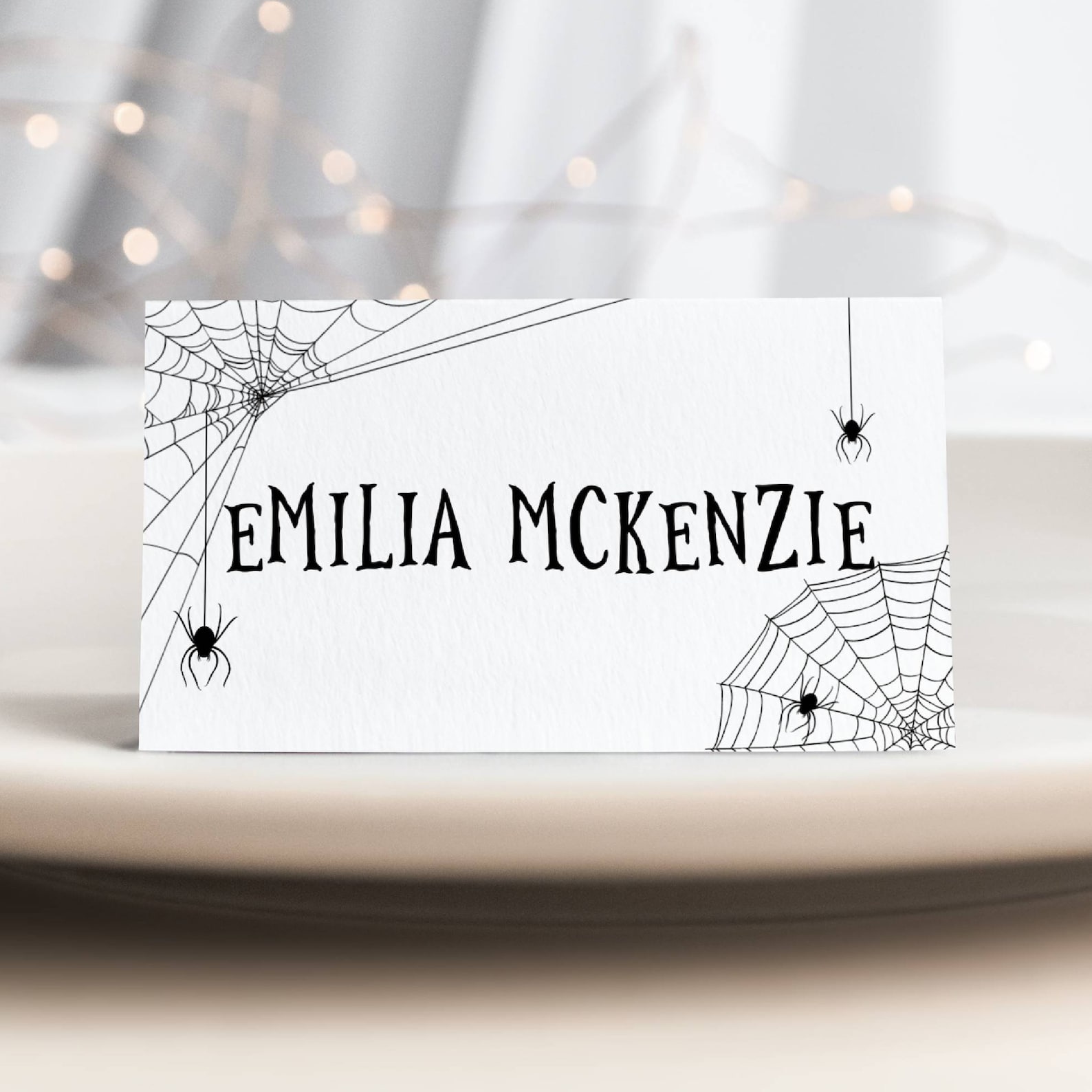 Fine Spiderwebs Around a White Tent Card White tent place card with black spiderweb corners and a guest name.