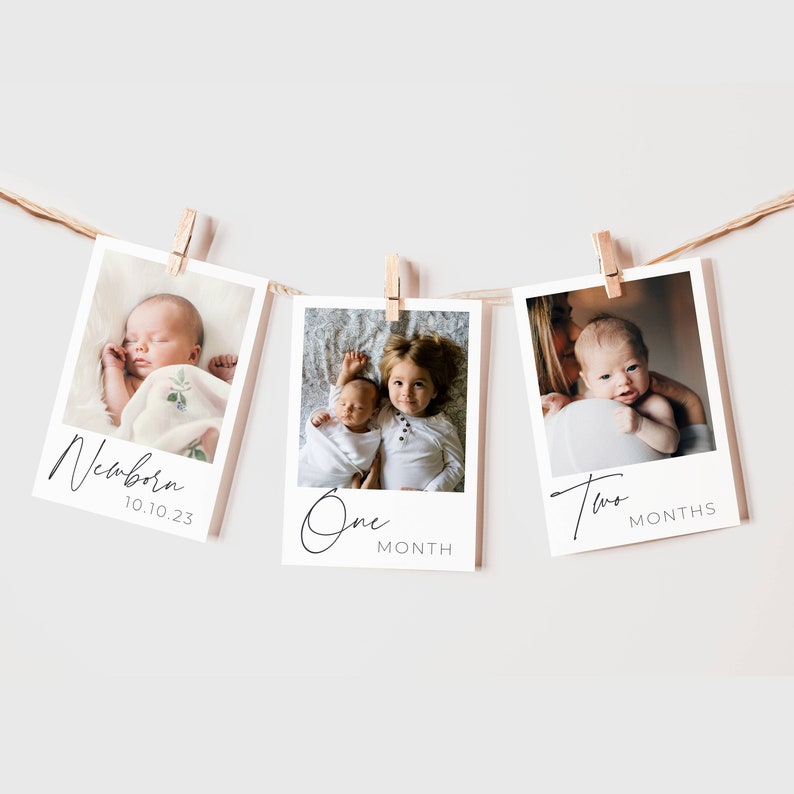 May include: Three white photo frames with black borders, hanging from a string with wooden clothespins. Each frame contains a photo of a baby at different ages, with the text "Newborn 10.10.23", "One Month", and "Two Months" written below the photos.
