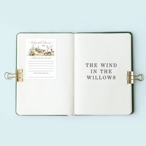 Pu&ograve; includere: Un diario verde con una pagina bianca aperta a un risguardo con un'illustrazione ad acquerello di una scena boschiva. Il risguardo ha il testo "baby's first library" e spazio per scrivere "scelto per te perch&eacute;" e "dato con amore da". La pagina opposta ha il titolo "Il vento tra i salici" scritto in nero.