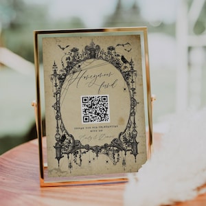 May include: A black and white illustration of a spooky, gothic frame with a QR code in the center. The text "Honeymoon Fund" is written in a decorative font. The text "Thank you for celebrating with us! Emily & Dominic" is written below the QR code.