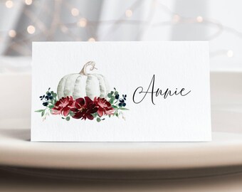 May include: White pumpkin with burgundy and blue floral accents on a place card with the name "Annie" written in black calligraphy.