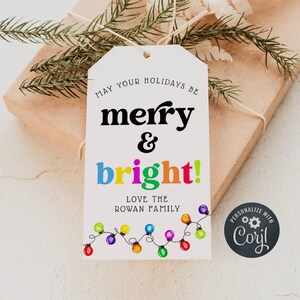 May include: White gift tag with the text "May your holidays be merry & bright!" in black and colorful letters. The tag also features a string of colorful lightbulbs and the text "Love the Rowan Family". A black circle with the text "Personalize with Coril" is in the bottom right corner.