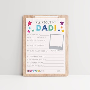 May include: A wooden clipboard holding a white questionnaire titled ALL ABOUT MY DAD. The sheet features colorful stars, blank lines for writing, and a gray square frame labeled HERE IS MY DAD with an arrow pointing to it. The bottom reads I LOVE YOU!