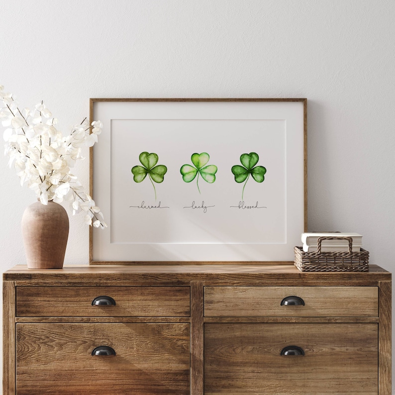 May include: A framed print with three watercolor shamrocks, each with the words "charmed", "lucky", and "blessed" written underneath.
