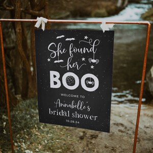 Könnte beinhalten: Ein schwarz-weißes Schild mit dem Text "She found her BOO" mit Spinnen- und Fledermaus-Illustrationen. Das Schild zeigt auch "Welcome to Annabelle's bridal shower 10.28.24".