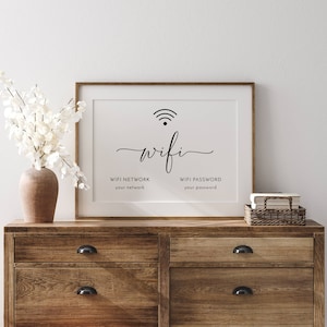 May include: A framed white print with the word "wifi" in elegant script, a wifi symbol, and prompts for network and password. The print is displayed on a wooden dresser with a vase of white flowers.