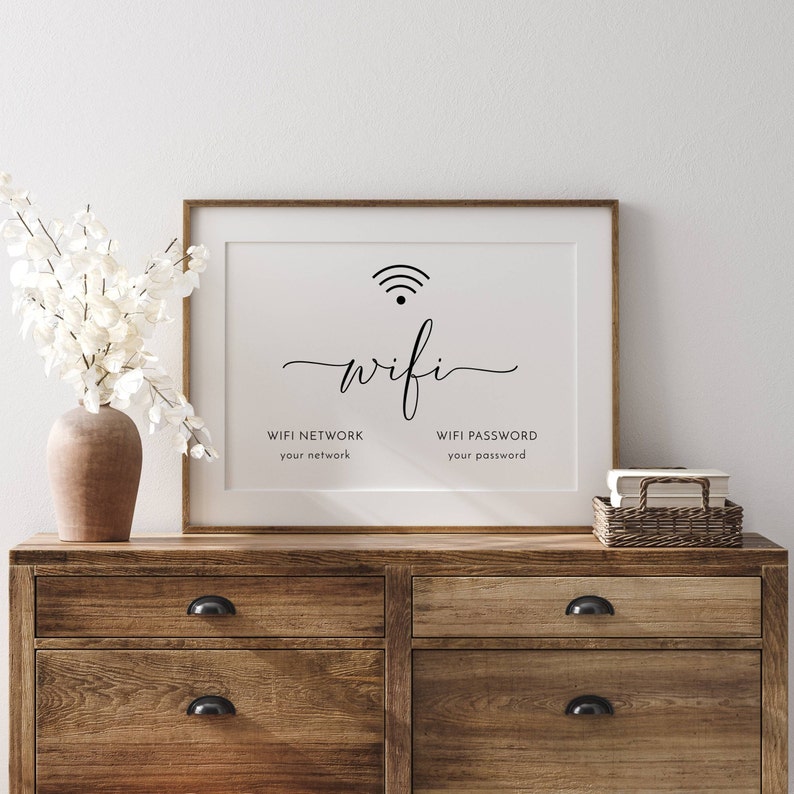 May include: A framed white print with the word "wifi" in elegant script, a wifi symbol, and prompts for network and password. The print is displayed on a wooden dresser with a vase of white flowers.