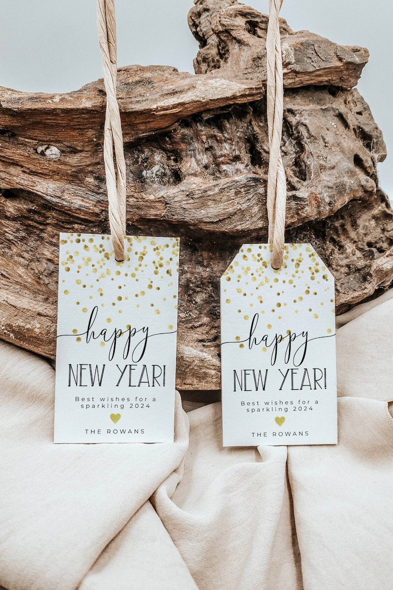 Puede incluir: Dos etiquetas de regalo blancas con confeti dorado y texto negro que dice "happy NEW YEAR!"  Los mejores deseos para un 2024 brillante.  The Rowans.