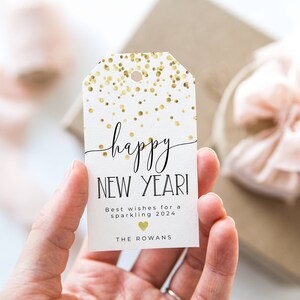Puede incluir: Etiqueta de regalo blanca con confeti dorado y texto negro que dice "happy NEW YEAR!" Los mejores deseos para un 2024 brillante. The Rowans.