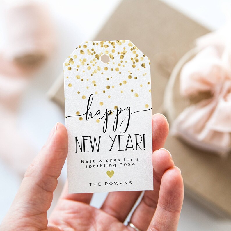 Puede incluir: Etiqueta de regalo blanca con confeti dorado y texto negro que dice "happy NEW YEAR!" Los mejores deseos para un 2024 brillante. The Rowans.