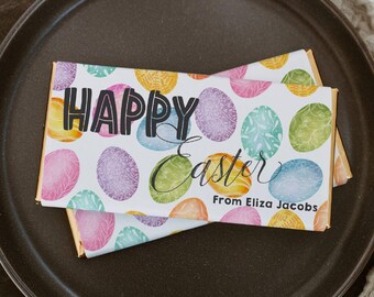 May include: A white chocolate bar wrapper with a colorful Easter egg pattern. The wrapper says "Happy Easter" and "From Eliza Jacobs".