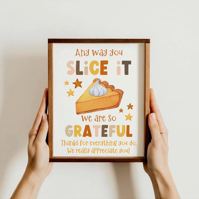 Puede incluir: Una impresi&oacute;n enmarcada con un tema de Acci&oacute;n de Gracias. La obra de arte presenta el texto "Any way you slice it, we are so grateful". Tambi&eacute;n se incluyen una porci&oacute;n de pastel e ilustraciones de estrellas. El marco es de color marr&oacute;n c&aacute;lido.