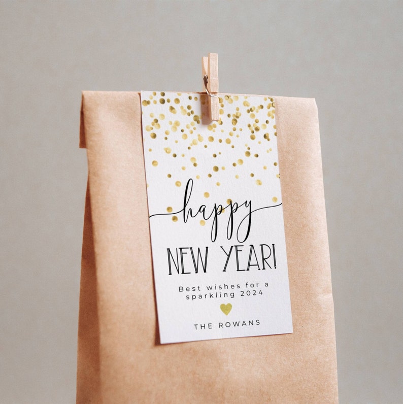 Puede incluir: Una etiqueta de regalo blanca con confeti dorado y el texto "happy new year!"  Los mejores deseos para un 2024 brillante. The Rowans.