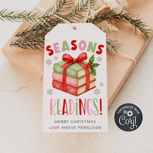 May include: A white gift tag with the words "SEASONS READINGS!" in red and pink. The tag features a stack of books tied with a red bow and holly. The text "MERRY CHRISTMAS LOVE MAEVE FERGUSON" is printed at the bottom. A small circular logo is in the bottom right corner.