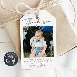 May include: White thank you tag with a photo of a baby boy in a blue and white outfit. The tag says "Thank you for making my birthday so special! Love Archie".