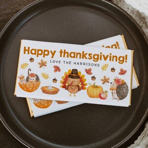 May include: White chocolate bar with a Thanksgiving theme. The bar features a turkey, a pumpkin, a pie, and two hedgehogs. The text on the bar reads "Happy Thanksgiving! Love the Harrisons".