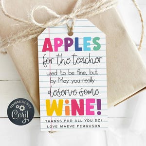 May include: A white gift tag with a pink line at the top and blue lines throughout. The text on the tag reads "APPLES for the teacher used to be fine, but by May you really deserve some WINE! THANKS FOR ALL YOU DO! LOVE MAEVE FERGUSON".