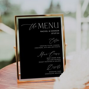 May include: A black framed menu board with gold trim, listing the menu for a wedding reception. The menu includes appetizers, main courses, and desserts. The text on the menu board reads "The Menu", "Rachel & Connor", "07.07.24", "Extre", "Grazing Plate: Cheese, Crackers, Dip and Antipasto", "Main Courses", "Beef Spare Ribs", "Grilled Salmon", "Roast Potatoes & Salads", "Desserts", "Wedding Cake", and "Chocolate Mousse".