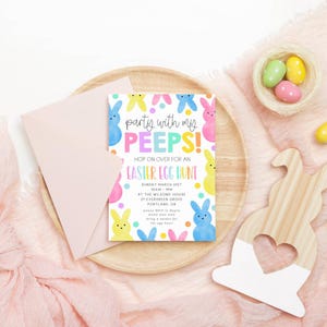 May include: An Easter-themed invitation with the text "Party with my PEEPS!" and "Easter Egg Hunt." The invitation is surrounded by colorful bunny illustrations and rests on a wooden tray with a pink envelope. A wooden bunny cutout and a nest with Easter eggs are also present.