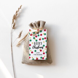 May include: A white gift tag with a red, green, and gold confetti pattern. The tag says "Merry Christmas" and "Love The Rowans".