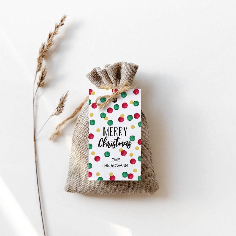 May include: A white gift tag with a red, green, and gold confetti pattern. The tag says "Merry Christmas" and "Love The Rowans".