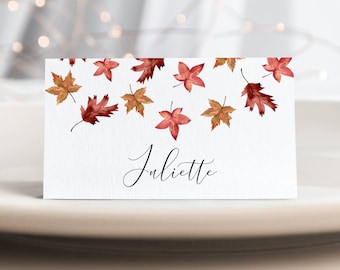 May include: A white place card with an autumn theme. The card has a border of red and orange leaves and the name "Juliette" written in black cursive.