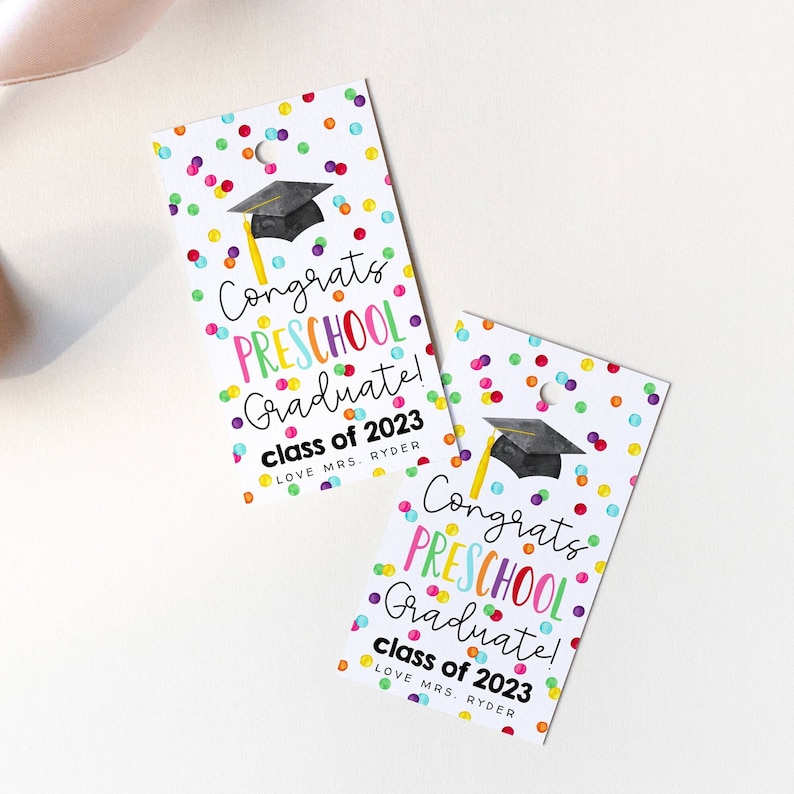 Puede incluir: Dos etiquetas de regalo blancas con confeti de colores y un gorro de graduaci&oacute;n negro. El texto en las etiquetas dice "&iexcl;Felicidades graduado de preescolar! Clase de 2023 Con cari&ntilde;o de la Sra. Ryder".