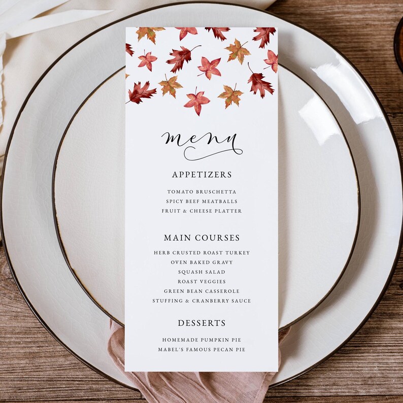 May include: A white menu card with a fall leaf design, featuring appetizers, main courses, and desserts. The menu is set on a white plate with a wooden background. The menu includes items like roast turkey and pumpkin pie.