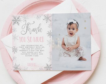 Puede incluir: Un plato de papel rosa contiene una tarjeta plegada y un sobre. La tarjeta presenta una foto de un bebé y el texto "Thank You So Much" con un mensaje sobre un primer cumpleaños. La tarjeta está decorada con copos de nieve.