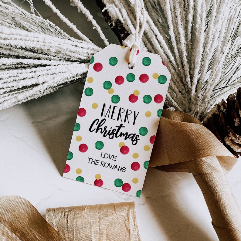 May include: A white gift tag with a red, green, and yellow polka dot pattern. The tag says "Merry Christmas" in black cursive lettering and "Love The Rowans" in black lettering.